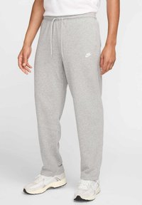 Pantalons de survêtement gris en tissu doux, avec une taille à cordon, des poches latérales et un petit logo Nike blanc sur la cuisse gauche.