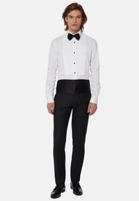 Chemise de smoking blanche à devant plissé et nœud papillon noir, assortie à un pantalon noir taille haute et des chaussures noires brillantes.