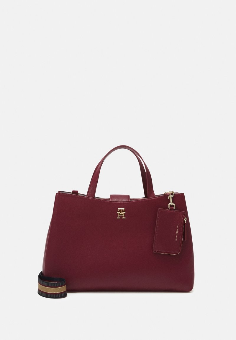 Sac à main en cuir bordeaux avec deux poignées, logo doré, pochette assortie attachée et bandoulière rayée amovible sur fond blanc.