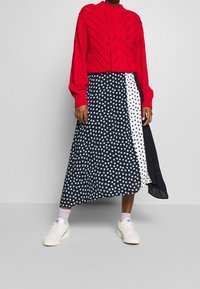 Suéter de punto rojo con diseño texturizado, combinado con una falda midi asimétrica de varios patrones en negro y blanco con lunares azules.