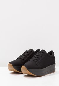 Musta kangastennarit pyöreällä kärjellä, teksturoidulla päällisellä ja paksulla, tummalla pohjalla. Varustettu purukumipohjalla, joka tarjoaa hyvän pidon.