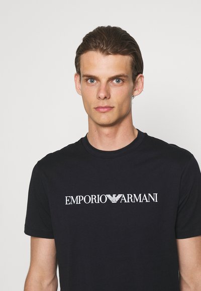 Black cotton t-shirt with a crew neck and short sleeves. Features white "EMPORIO ARMANI" logo on the front. Smooth texture, fitted design.