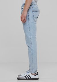 Világosk�ék, slim fit farmernadrág sima textúrával, öt zsebes kialakítással és diszkrét kopott hatással. Fekete-fehér sportcipővel párosítva.