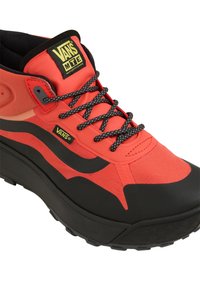 Punainen ja musta korkeavartinen lenkkari, jossa on synteettinen päällinen, teksturoitu kangas, paksu pohja, mustat nauhat sekä Vans-logo kielen ja sivun kohdalla.