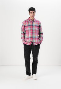 Plaid shirt in pink, blue, and green tones with long sleeves, button closure, and chest pocket; paired with black pants and white sneakers.