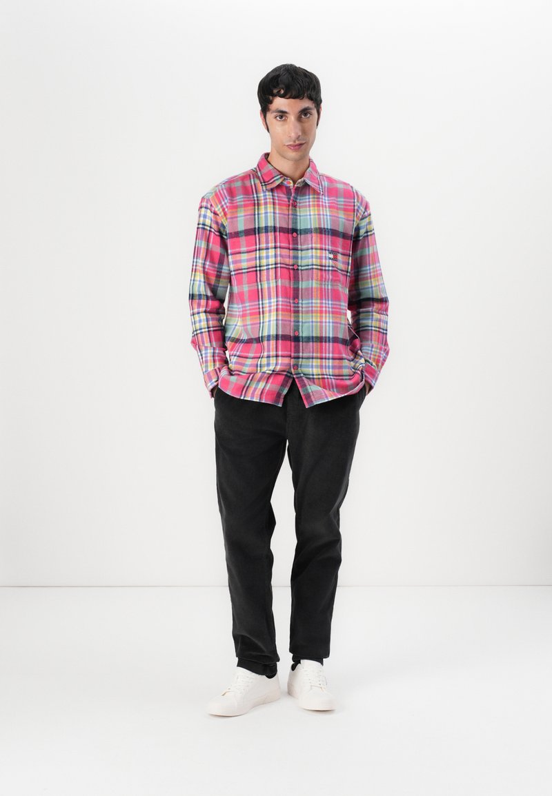 Geruite shirt in roze, blauw en groene tinten met lange mouwen, knoopsluiting en borstzak; gecombineerd met zwarte broek en witte sneakers.
