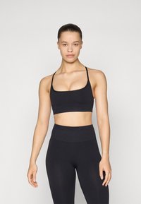 Sujeción deportiva negra con tirantes finos y escote redondeado, combinada con leggings negros de cintura alta. Ambas prendas tienen una textura suave.