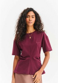 Bordowa bluzka z krótkim rękawem o luźnym kroju, z subtelnym haftem imitującym rzęsy i gładką bawełnianą fakturą.