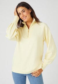 Suéter amarillo claro con un cuello con media cremallera, mangas abullonadas y texturizadas. Cuenta con un cuello y dobladillo acanalados.