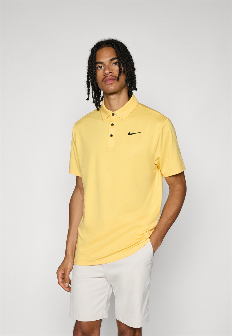 Ανδρικό κίτρινο πόλο μπλουζάκι από μείγμα βαμβακιού, με τρεις κουμπάκια, μαύρο λογότυπο Nike και κοντά μανίκια, σε συνδυασμό με λευκές βερμούδες.