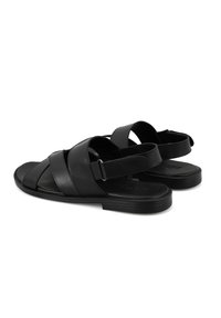 Schwarze Leder-Sandalen mit mehreren gekreuzten Riemen und einem hinteren Knöchelriemen, ausgestattet mit einer flachen Gummisohle und einem strukturierten Fußbett.