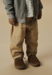 Pantaloni in lino beige con finitura testurizzata, abbinati a una giacca a zip in maglia grigia e scarpe stringate in suede marrone.