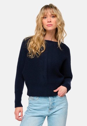 Pull en maille bleu marine avec une coupe ample, des poignets et un ourlet côtelés. La texture est douce et épaisse, avec un design simple et un col rond.
