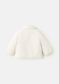 Bela prešita jakna z ovratnim izrezom, raglanskimi rokavi in ohlapnim krojem. Teksturirana tkanina z nežnimi detajli na zadnji strani.