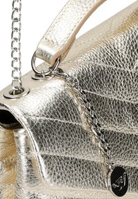 Borsa in metallo dorato con texture trapuntata, manici in catena e pelle, occhielli circolari e un charm decorativo in metallo attaccato.