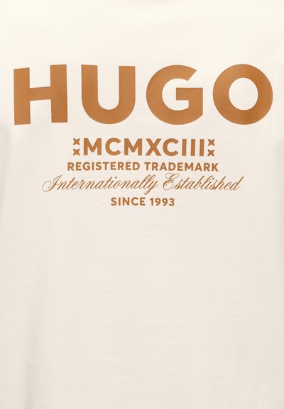Логото HUGO с големи кафяви букви над римските цифри MCMXCIII, текст „Регистрирана търговска марка“, „Международно установена“ и „От 1993“ на кремав фон.