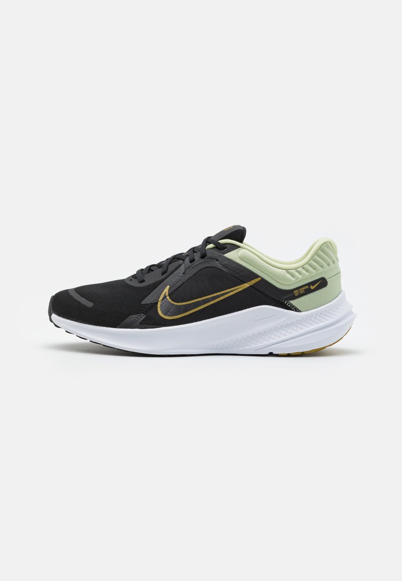 Chaussure de sport noire avec une tige en mesh, des accents dorés, un talon vert clair, et une semelle extérieure blanche avec des détails texturés, conçue pour le confort et le soutien.