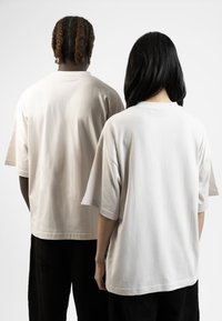 Light beige oversized t-shirts with short sleeves, cotton material, featuring a crew neck design. Back view shows smooth texture and simplicity.