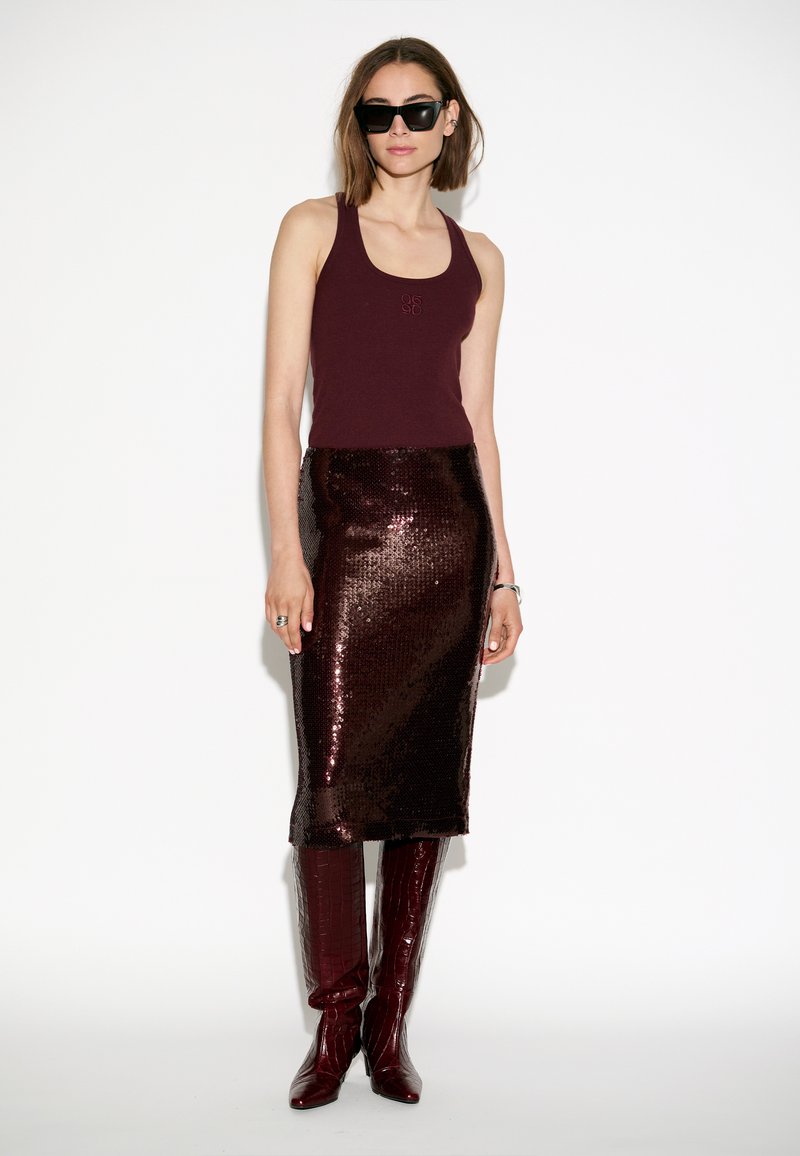 Bordeaux tanktop, glanzende bordeaux paillettenrok, kniehoge patenten laarzen met krokodillenpatroon, zonnebril, minimale accessoires.