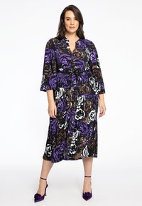 Lang kjole med blomsterprint i lilla, sort og brune farver. Materialet virker let; inkluderer bælte og knapper foran.