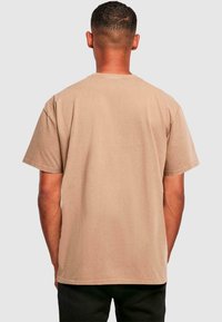T-shirt med korte ærmer og rund hals i lys beige bomuld. Har en afslappet pasform, enkelt design og subtil tekstur. Ingen grafik eller detaljer synlige.