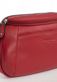 Borsa rossa in pelle con finitura testurizzata, dotata di chiusura con zip superiore e logo impresso. Forma compatta e arrotondata con design minimalista.