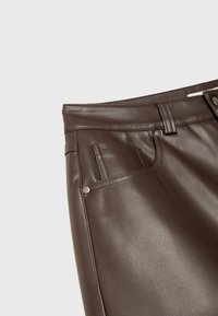 Pantalon en similicuir marron avec une texture lisse, un design à cinq poches, des coutures visibles et des accents métalliques sur les bords des poches.
