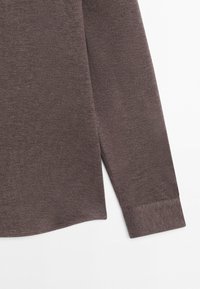 Brun skjortærme med lange ærmer og manchet i et subtilt struktureret stof, vist på en hvid baggrund.