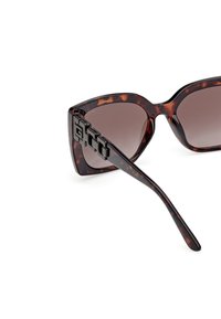 Gafas de sol tipo ojo de gato en carey, con lentes oscuros y un chunky detalle de metal negro en las patillas. Montura de plástico suave.