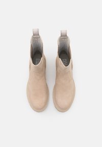 Béžové semišové kotníkové boty s elastickými bočními panely, poutky na patě a zaoblenou špičkou, s texturovanou podrážkou a diskrétním logem uvnitř.