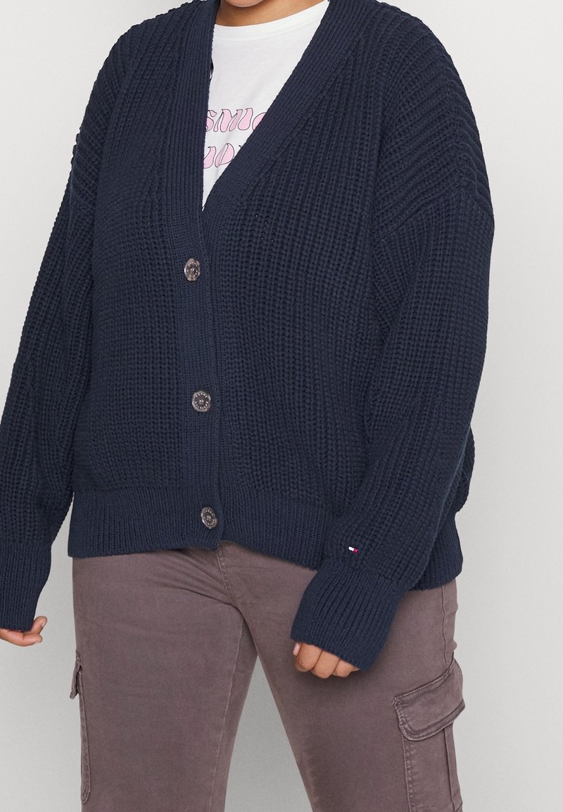 Marineblauer Strickcardigan mit lockerem Sitz, tiefem V-Ausschnitt und großen Knöpfen. Mit gerippten Bündchen und Saum sowie einem Tommy Hilfiger Logo-Akzent.