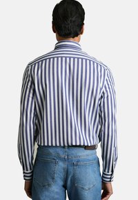 Camisa a rayas con rayas verticales en azul marino y blanco, mangas largas, un cuello ajustado y un corte relajado, combinada con jeans de un azul claro.