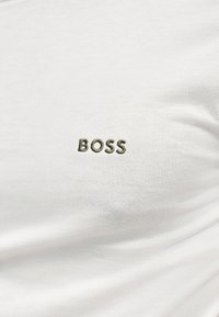 Tissu blanc avec le mot "BOSS" brodé en fil foncé au centre.