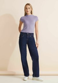 Ljuslila kortärmad topp med en figurnära silhuett, kombinerad med mörkblå raka jeans. Vita sneakers och minimalistisk design.