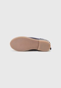 Semelle de chaussure en caoutchouc brun clair avec une surface texturée, un arc flexible et un matériau supérieur bleu visible sur le bord.