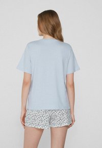 Světle modré tričko s krátkým rukávem a volným střihem, spárované s bílými šortkami s květinovým vzorem v modré a námořnické barvě.