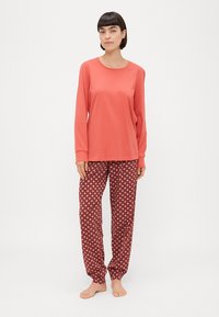 Roze shirt met lange mouwen, gecombineerd met maroon geklede pyjamabroek met kleine geometrische vormen, casual pasvorm en zachte materialen.