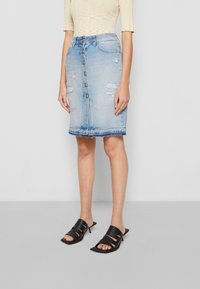 Denim rok, lichtblauw, knieholte-lengte, met voorste knopen, versleten details en een rafelige zoom. Gecombineerd met zwarte sandaaltjes met hakken en bandjes.