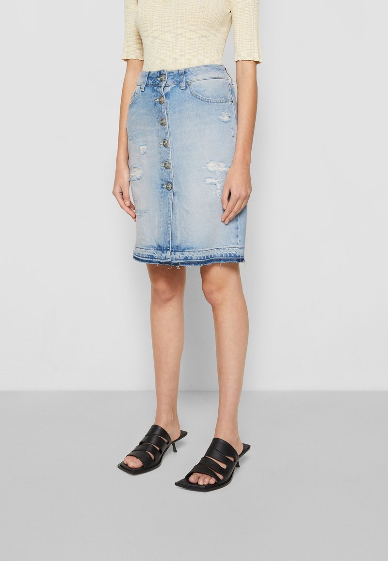 Denim rok, lichtblauw, knieholte-lengte, met voorste knopen, versleten details en een rafelige zoom. Gecombineerd met zwarte sandaaltjes met hakken en bandjes.