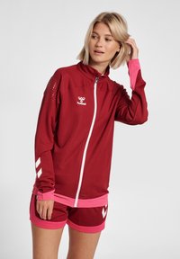 Chaqueta de cremallera color marr�ón con detalles y logotipo en rosa, combinada con shorts rosas con detalles en blanco. Tejido ligero con diseño texturizado.