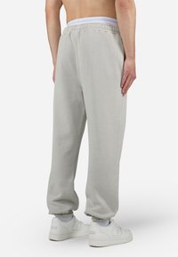 Pantalones de chándal gris claro fabricados en una mezcla de algodón, con un ajuste relajado, cinturilla elástica y dobladillos ajustados. Combinados con zapatillas blancas.