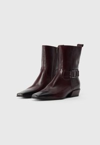 Bottines en cuir bordeaux avec un bout pointu, une fermeture éclair sur le côté et une boucle décorative. Elles possèdent un petit talon carré et une texture lisse.