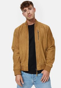 Brown suede bomber jacket with a zippered front, ribbed cuffs, and side pockets. Features a chest pocket with a metal zipper detail.