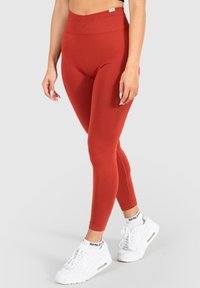 Leggings rossi a vita alta realizzati in tessuto elastico, con una superficie liscia e una forma aderente. Abbinate a scarpe da ginnastica bianche.