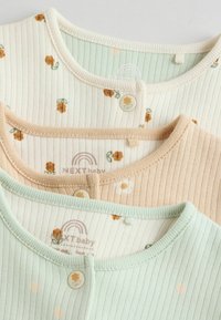 Tre baby toppe i ribbet stof: en lys grøn, en cremefarvet med blomsterprint og en ferskenfarvet med margueritter. Hver har en rund halsudskæring og knapper.