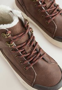 Braune Leder-Hochschuhe mit weißem Kunstfellfutter, braun-schwarz gesprenkelten Schnürsenkeln und Metallösen, mit einer strukturierten Oberfläche und Gummisohle.