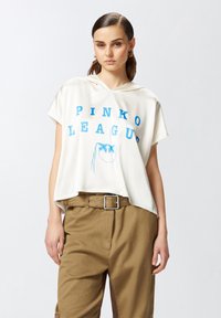 Felpa bianca a maniche corte con stampa blu "PINKO LEAGUE", dotata di tasca a canguro e vestibilità comoda, abbinata a pantaloni khaki.