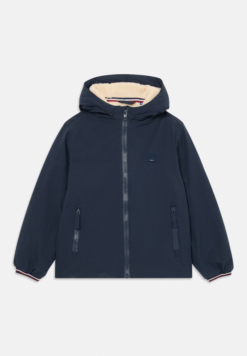Chaqueta con capucha en color navy, forrada con suave forro de lana beige, cierre frontal, dos bolsillos laterales y detalle de franjas en contraste en las mangas.