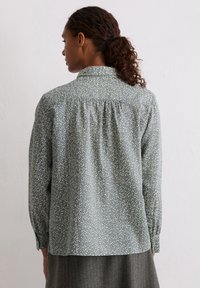 Jasnoniebieska kwiatowa koszula z kołnierzem, długimi rękawami, marszczonym tyłem oraz lekko luźnym krojem. Na całej powierzchni drobny wzór białych kwiatów.