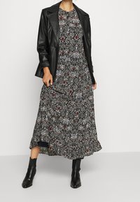 Mustat nahkatakki kukkakuosisella pitkällä mekolla tummilla sävyillä, punaisilla ja valkoisilla yksityiskohdilla, joka omaa virtaavan siluetin ja röyhelöreunuksen.